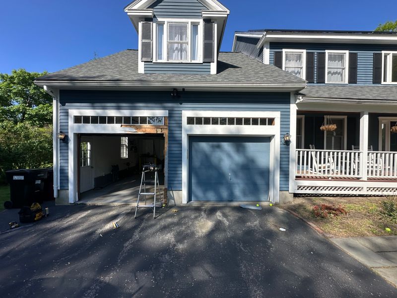 Dual white garage doors with transom windows being installed on blue colonial in MA